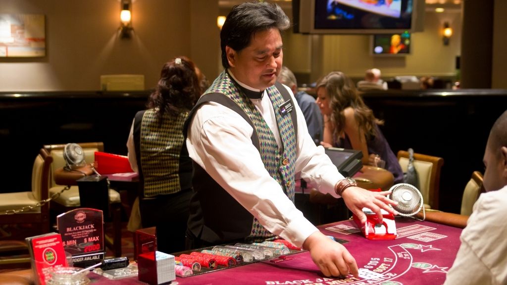 A casino croupier dealing cards at a blackjack table, highlighting the human oversight central to land-based casino operations.